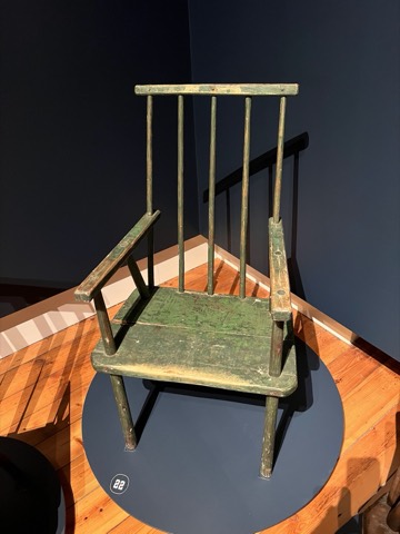 A tall green-painted armchair on a round museum plinth.