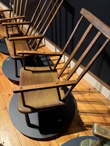 A tall-backed stick chair beside the Larcombe family wall text in the museum.