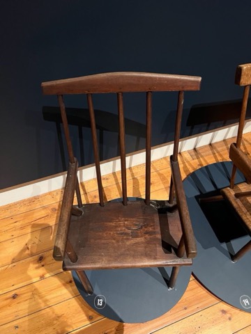 An antique chair with inverted armrests, against a deep navy museum wall.